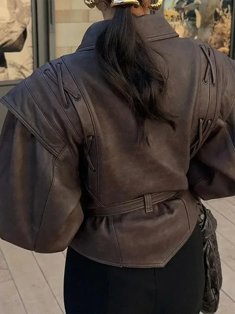 Person wearing a dark brown leather jacket with a belt, standing indoors.