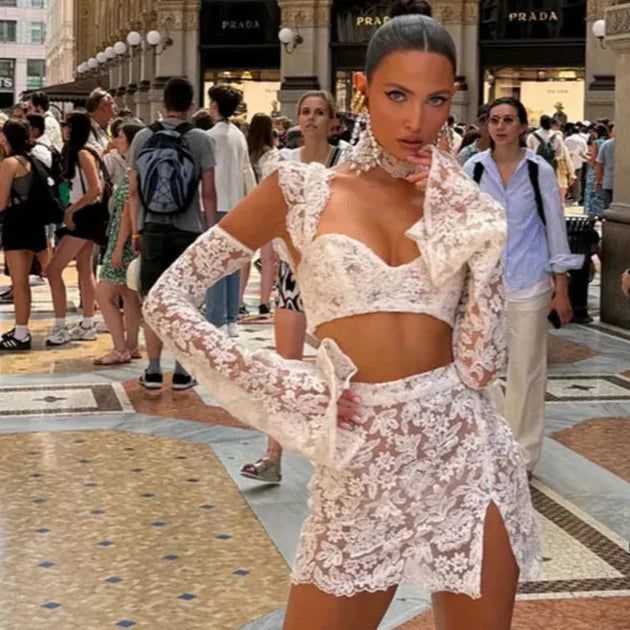 Woman in a white lace outfit standing in a busy urban setting with people around.