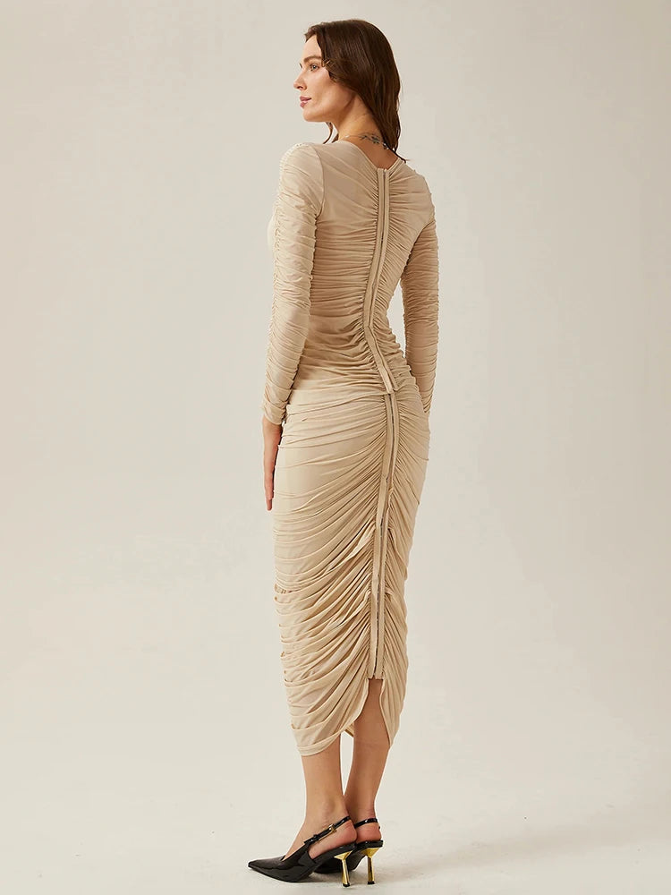 Woman wearing a beige long-sleeve dress with ruched details on a plain background