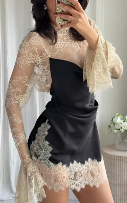 Person wearing a black dress with beige lace overlay in a neutral setting.