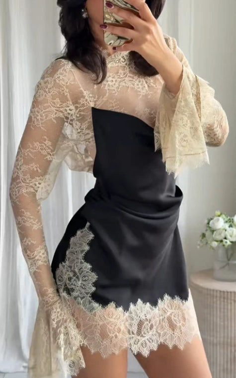 Person wearing a black dress with beige lace overlay in a neutral setting.