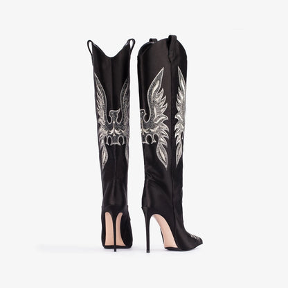 Black knee-high boots with silver winged creature design on a white background