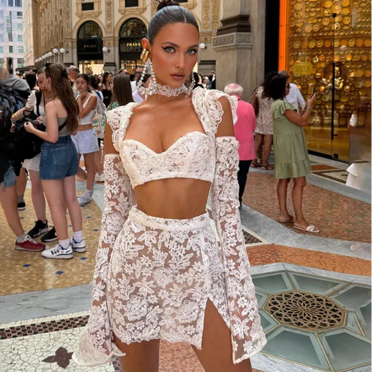 Woman in a white lace outfit standing in a busy indoor setting with people around.