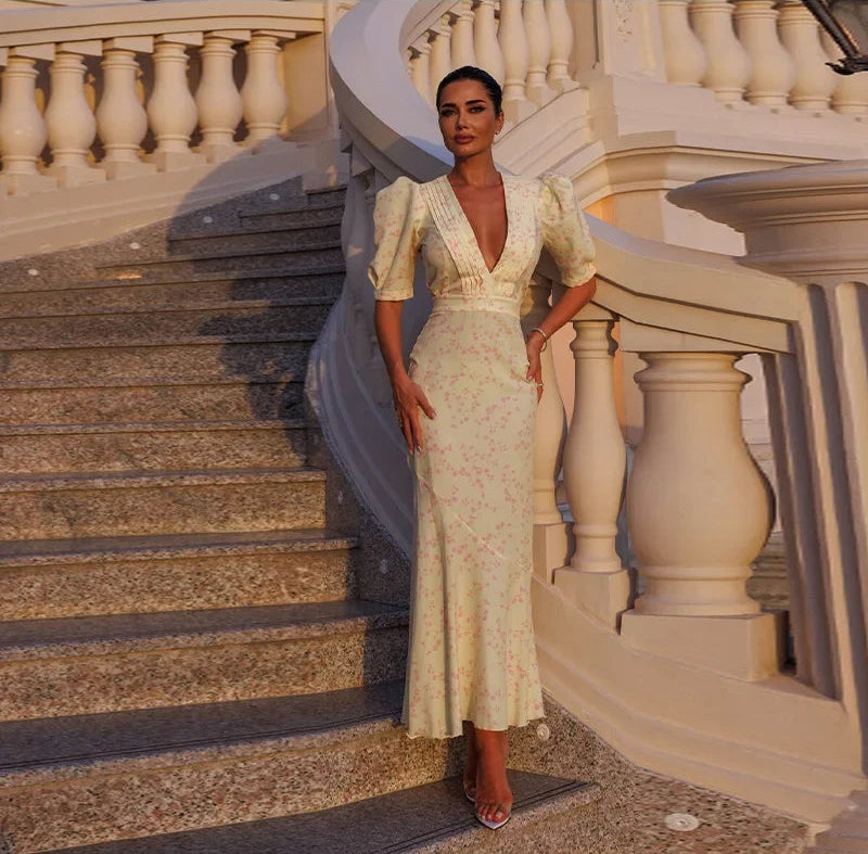 Woman in a floral dress standing on a staircase with decorative railings.