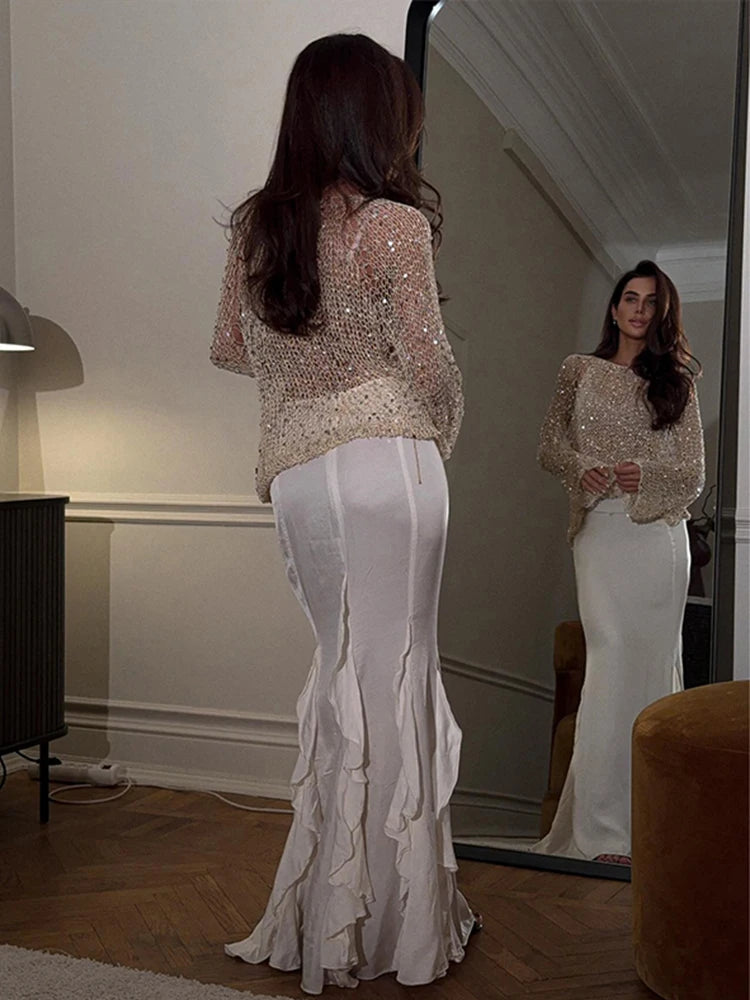 Woman wearing a sparkly top and white pants standing in front of a mirror.