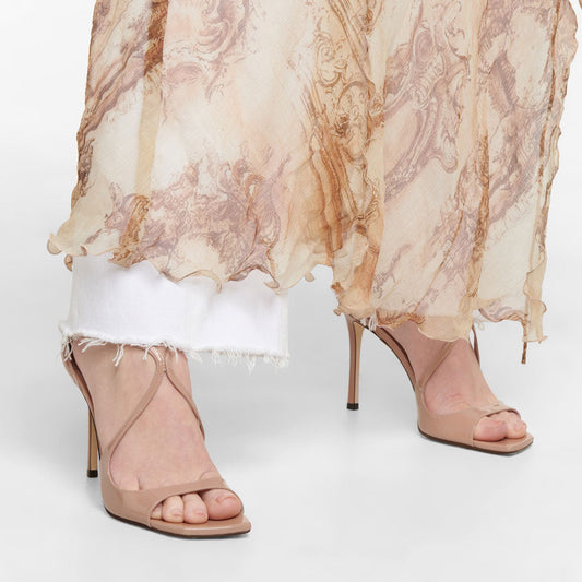 A pair of beige strappy square toe ankle strap stiletto sandals made of patent leather, displayed against a white background.