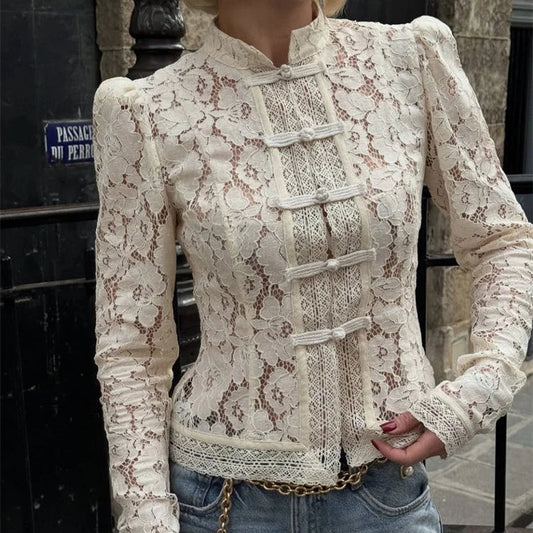Person wearing a lace top with long sleeves and jeans, standing against a stone wall.
