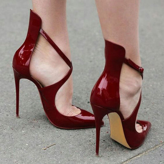 A pair of burgundy patent leather pointed toe stiletto pumps with crisscross straps on the vamp, viewed from the side.